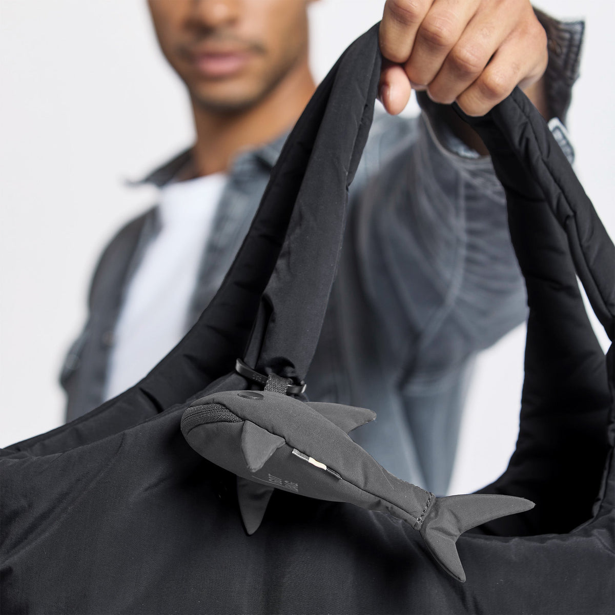 GOT BAG Shark Charm Taschenanhänger in Dunkelgrau, an einer Tasche, die ein Mann in der Hand hält