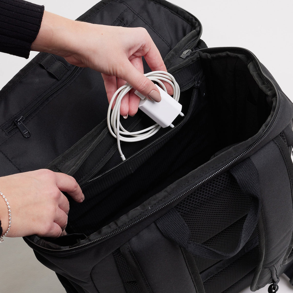 GOT BAG Pro Pack Laptoprucksack in Schwarz (Monochrome), eine Frau verstaut ein Ladekabel in der Innentasche